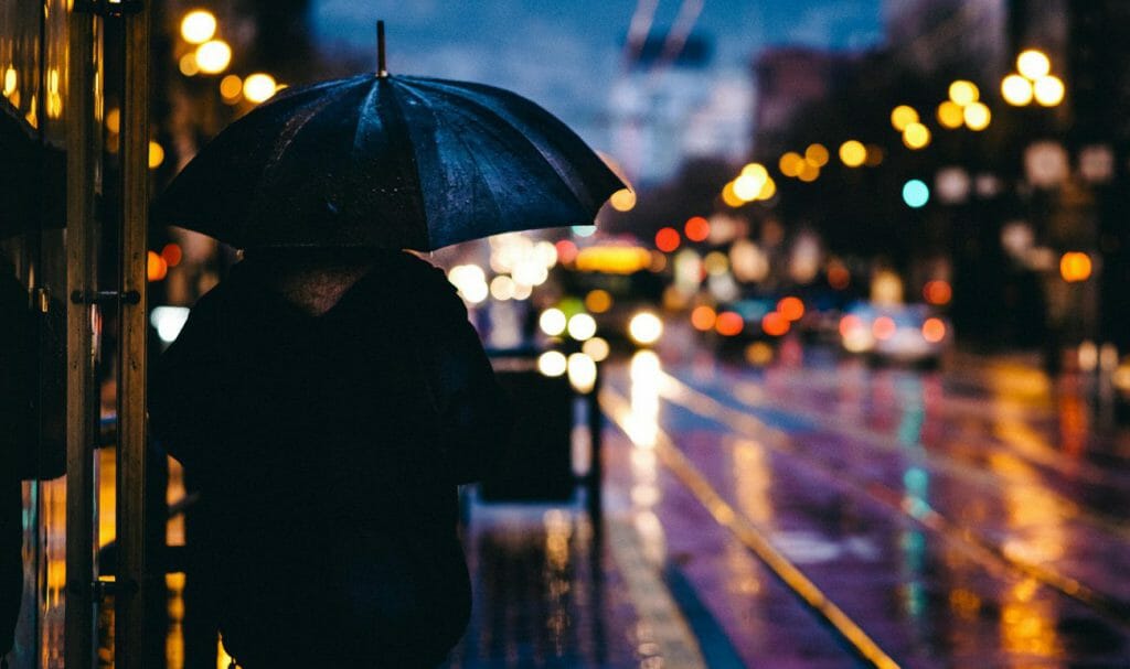 Una foto nocturna de cuadro completo de una persona bajo un paraguas mirando a una calle mojada