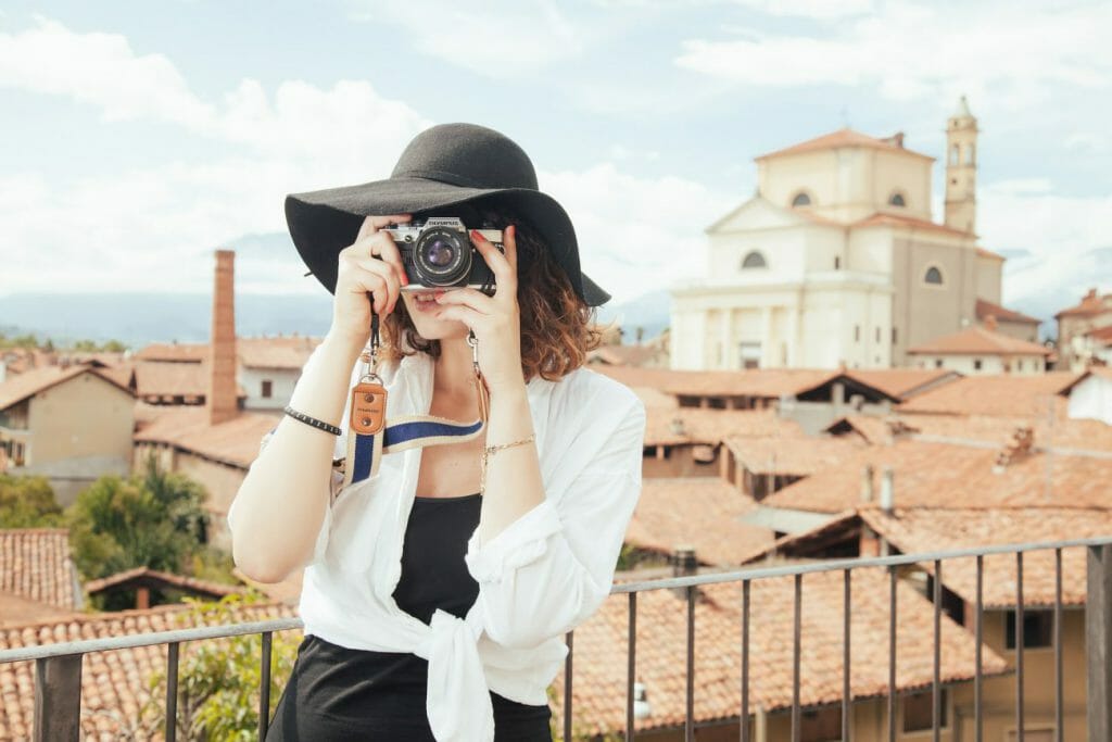 Una foto de una mujer con sombrero tomando una fotografía con una cámara.